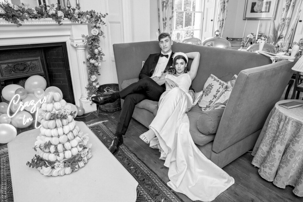 A real model couple dressed as a bride and groom and posing together on a sofa.